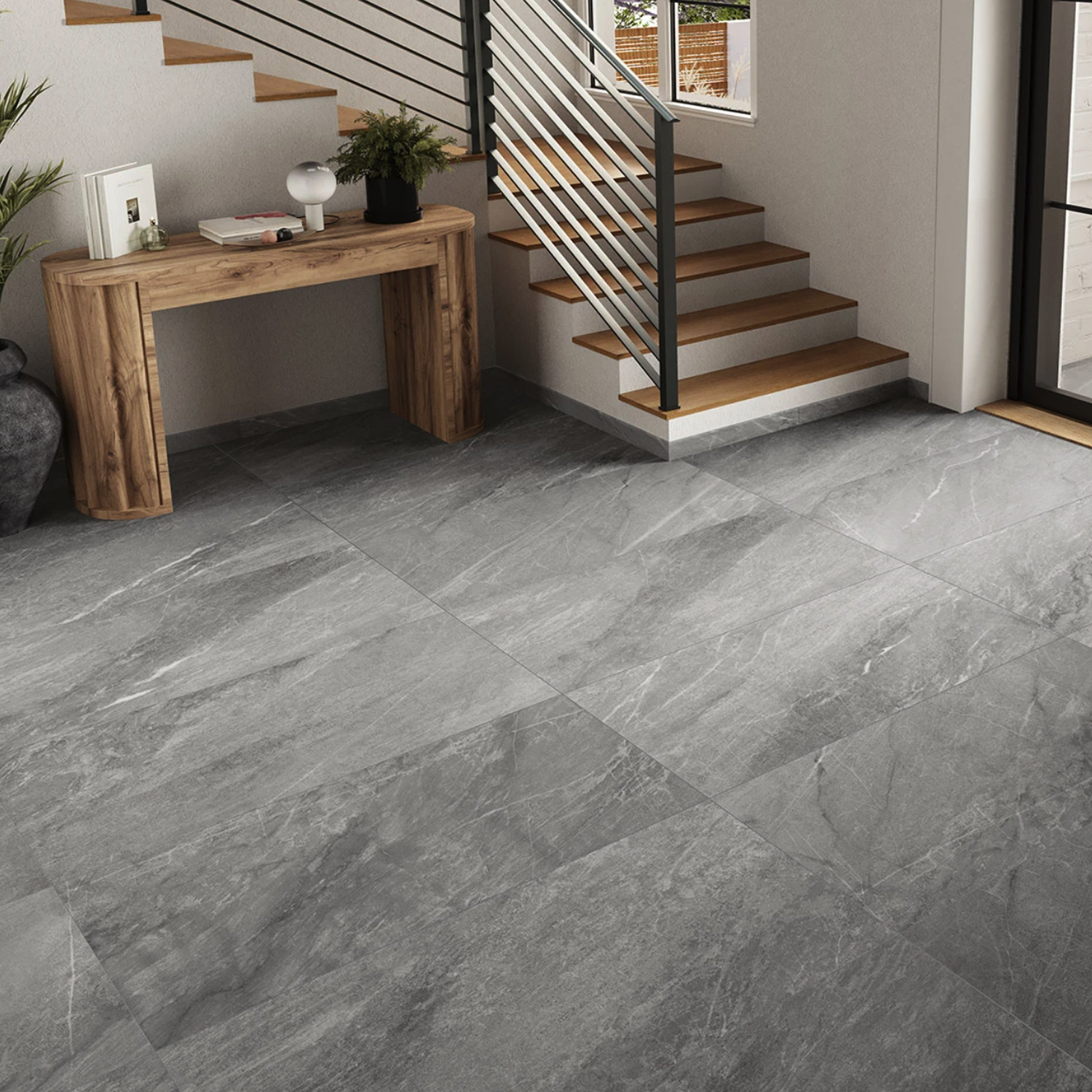 Modern entryway with large Legacy Marblestone - Steel gray tiles, a wooden console table with decor, stairs featuring wooden steps and a black railing, and a glass door letting in natural light.