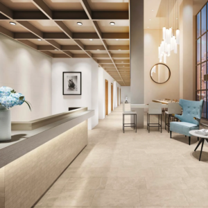 A modern hotel lobby featuring a Liberty - Monument Cream reception desk, elegant ceiling lights, a blue chair, tall windows, flowers in a vase, and a long hallway with doors along the left wall.