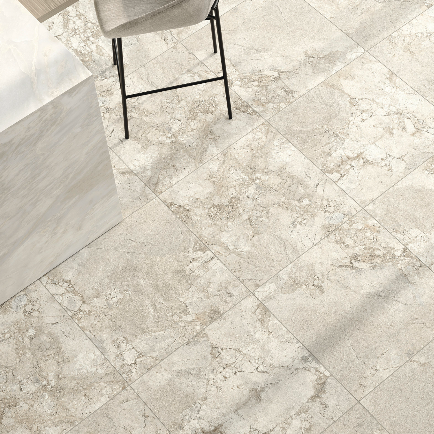 A contemporary floor featuring Lythos - Snow tiles in marble-like shades of beige and gray, complemented by a countertop and a single gray chair partially visible in the top left corner.