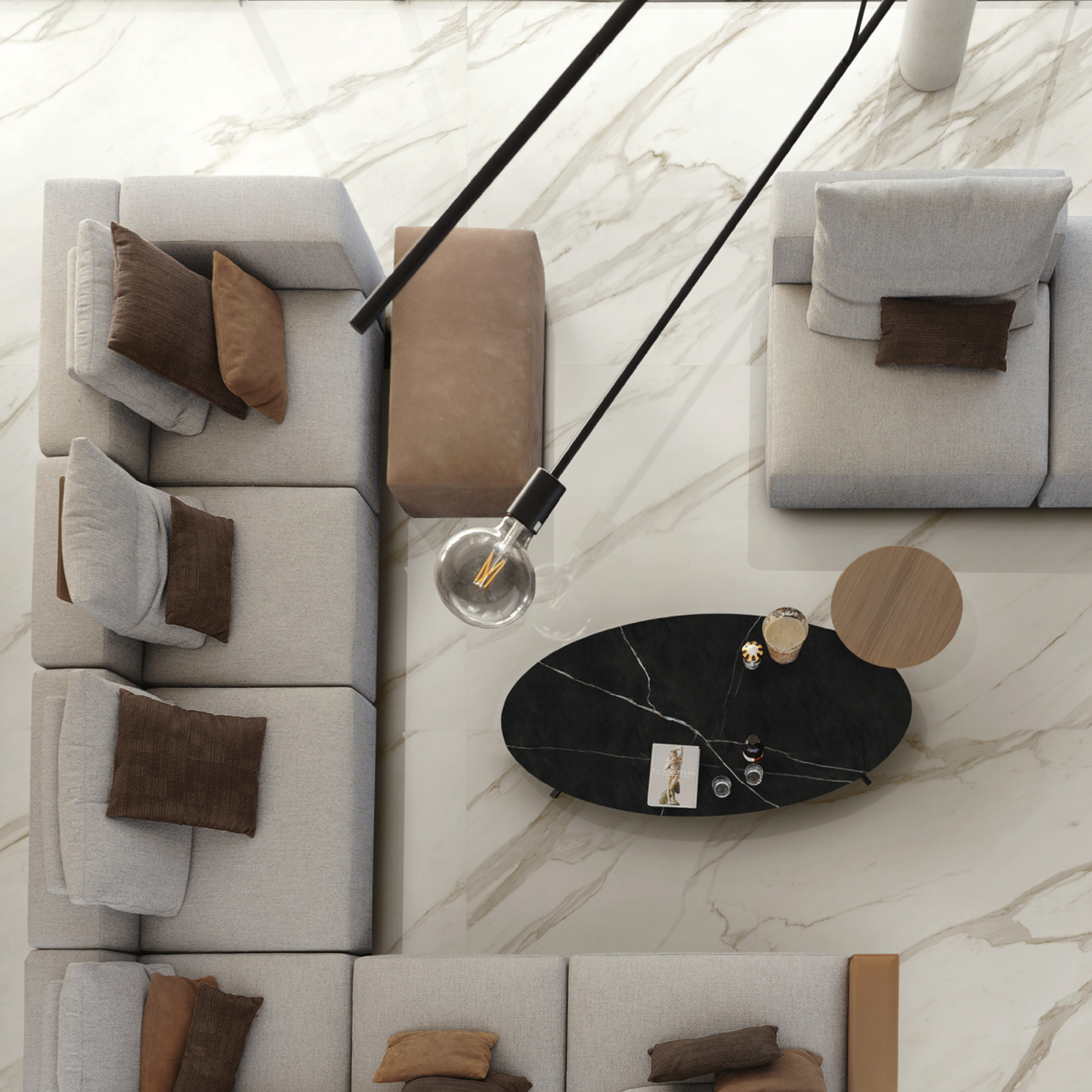 Modern living room with a gray sectional sofa, brown cushions, Marvel Meraviglia - Calacatta Bernini marble floor, black oval coffee table holding a magazine and glasses, and a hanging light bulb, viewed from above.
