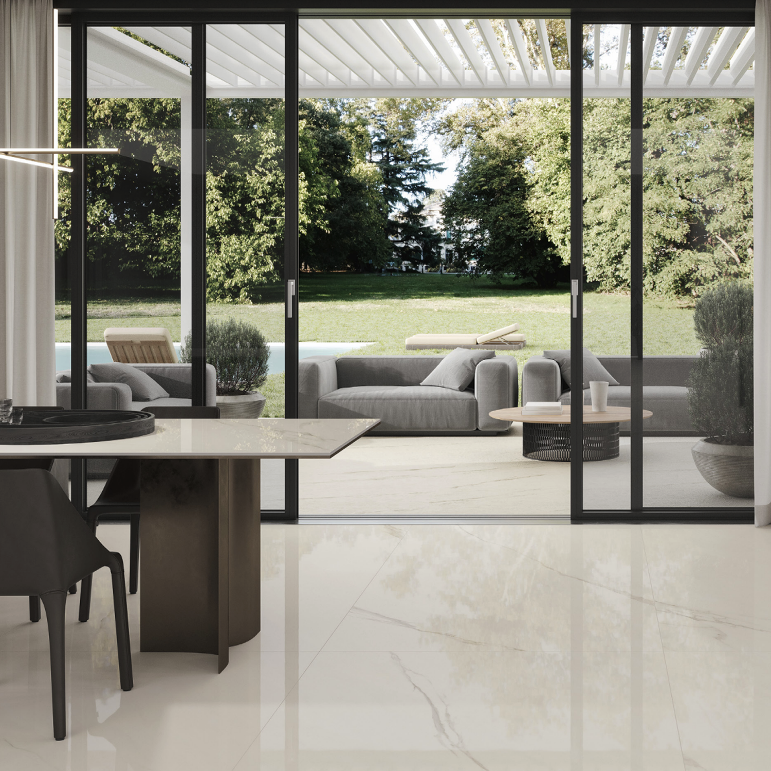 Modern dining room featuring Marvel Meraviglia - Calacatta Meraviglia marble flooring, with glass sliding doors that open to a patio furnished with gray outdoor furniture, potted plants, and a green lawn bordered by trees in the background.