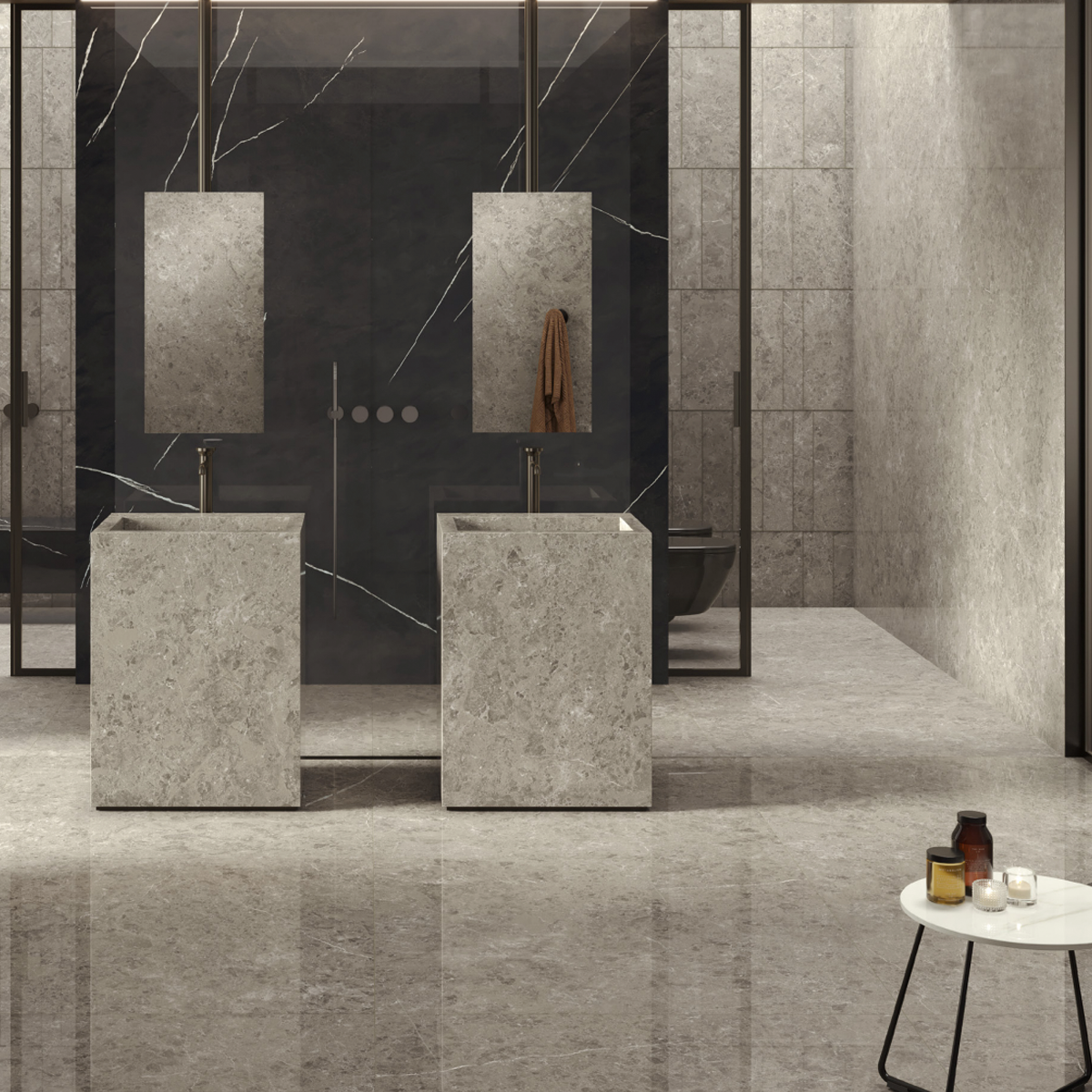 Modern bathroom featuring two stone pedestal sinks, rectangular mirrors, a striking Marvel Meraviglia - Grigio Elegante marble wall, glass showers, and a small round side table holding candles and jars. The space is minimalistic and elegant with neutral tones.