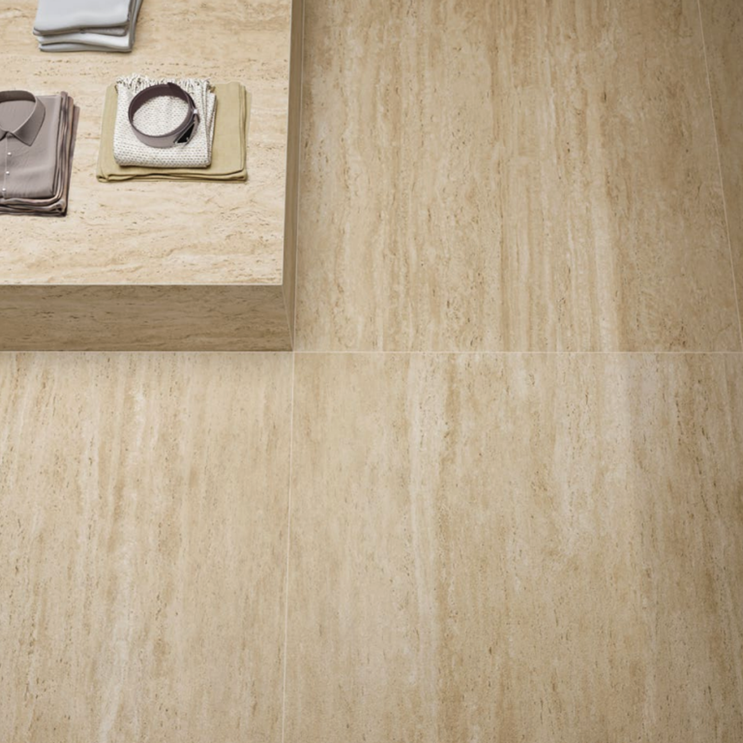 Folded towels and accessories rest on a beige stone ledge, complemented by Marvel Travertine - Sand Vein Cut large floor tiles featuring natural stone patterns.