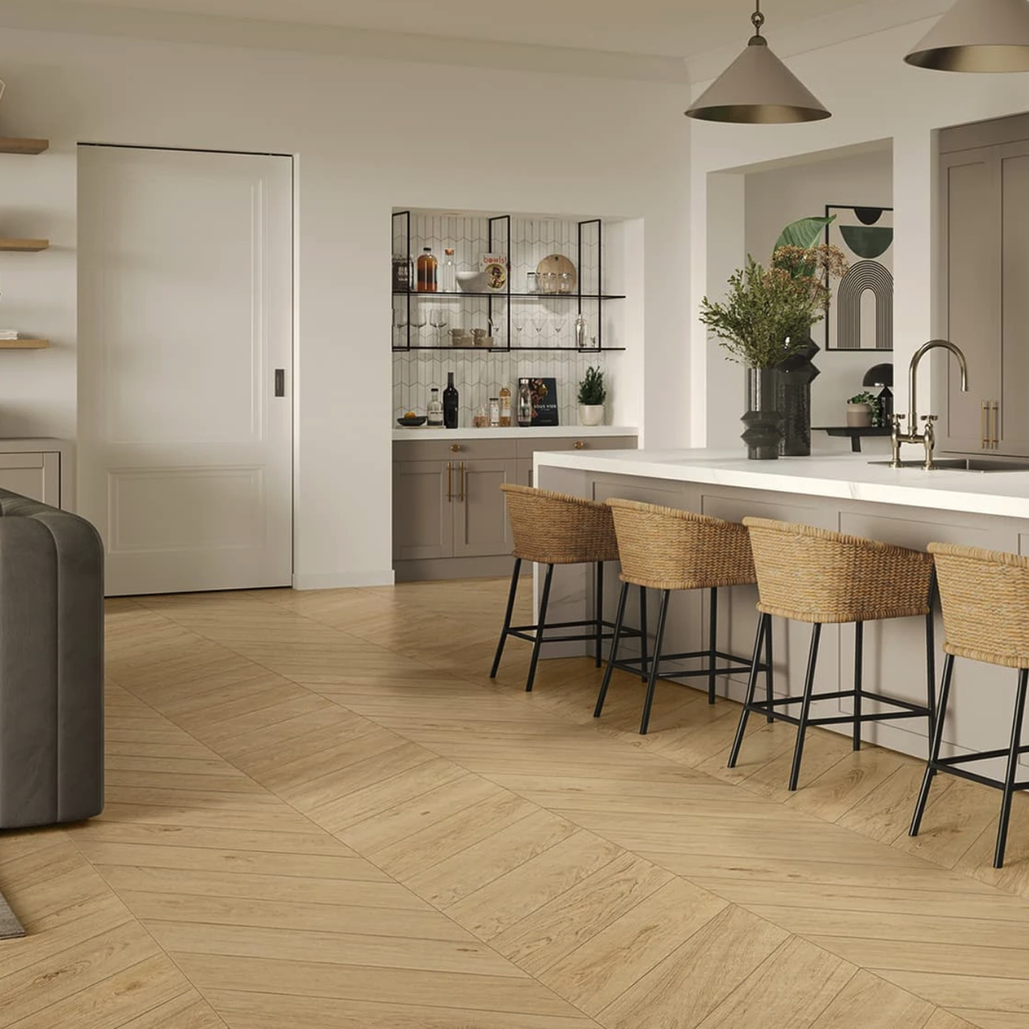 Modern kitchen featuring Memory Oak - Vanilla light wood floors, a white island with four wicker barstools, pendant lights, built-in shelves, and a bar area showcasing glassware and bottles. Neutral tones and minimalist décor throughout.