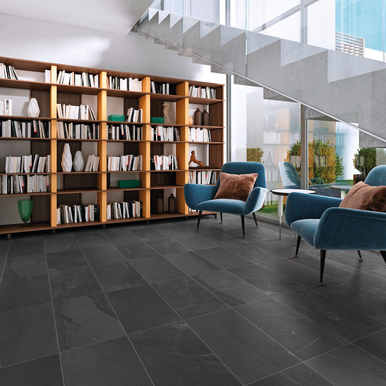 Modern reading area with tall bookcases, blue armchairs, brown pillows, and a glass staircase in a room with large windows and Modern Slate - Slate Charcoal tile flooring.