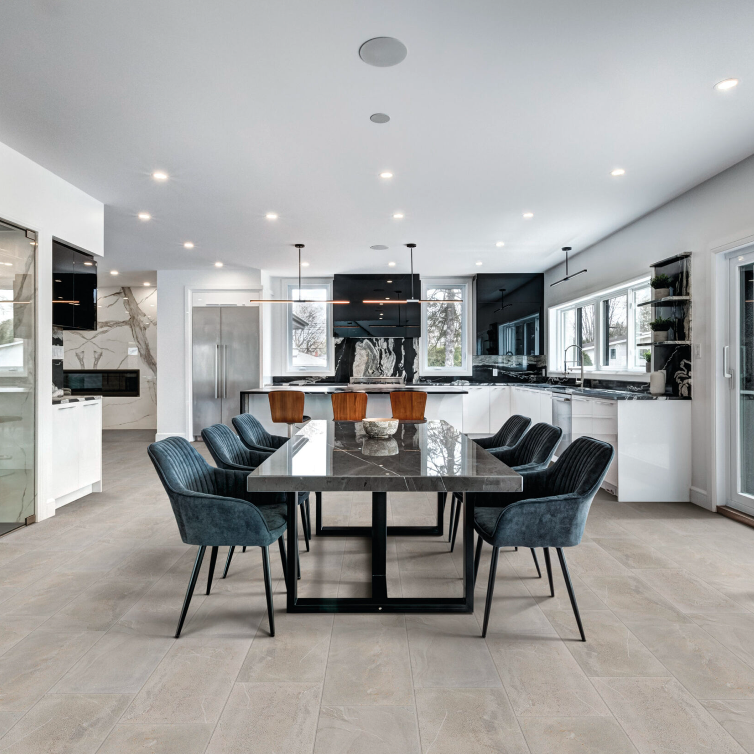 Modern kitchen and dining area featuring a Modern Slate - Slate Ivory table, eight dark upholstered chairs, white cabinets, stainless steel appliances, and large windows that fill the space with natural light.