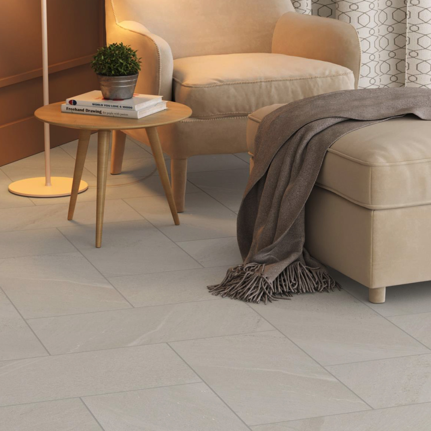 A cozy living room corner with a beige armchair, matching ottoman draped with a brown throw, round wooden side table holding a small plant and a book, floor lamp, and curtains with a geometric pattern. The pale tile floor is finished in Moonstone - Off-White.