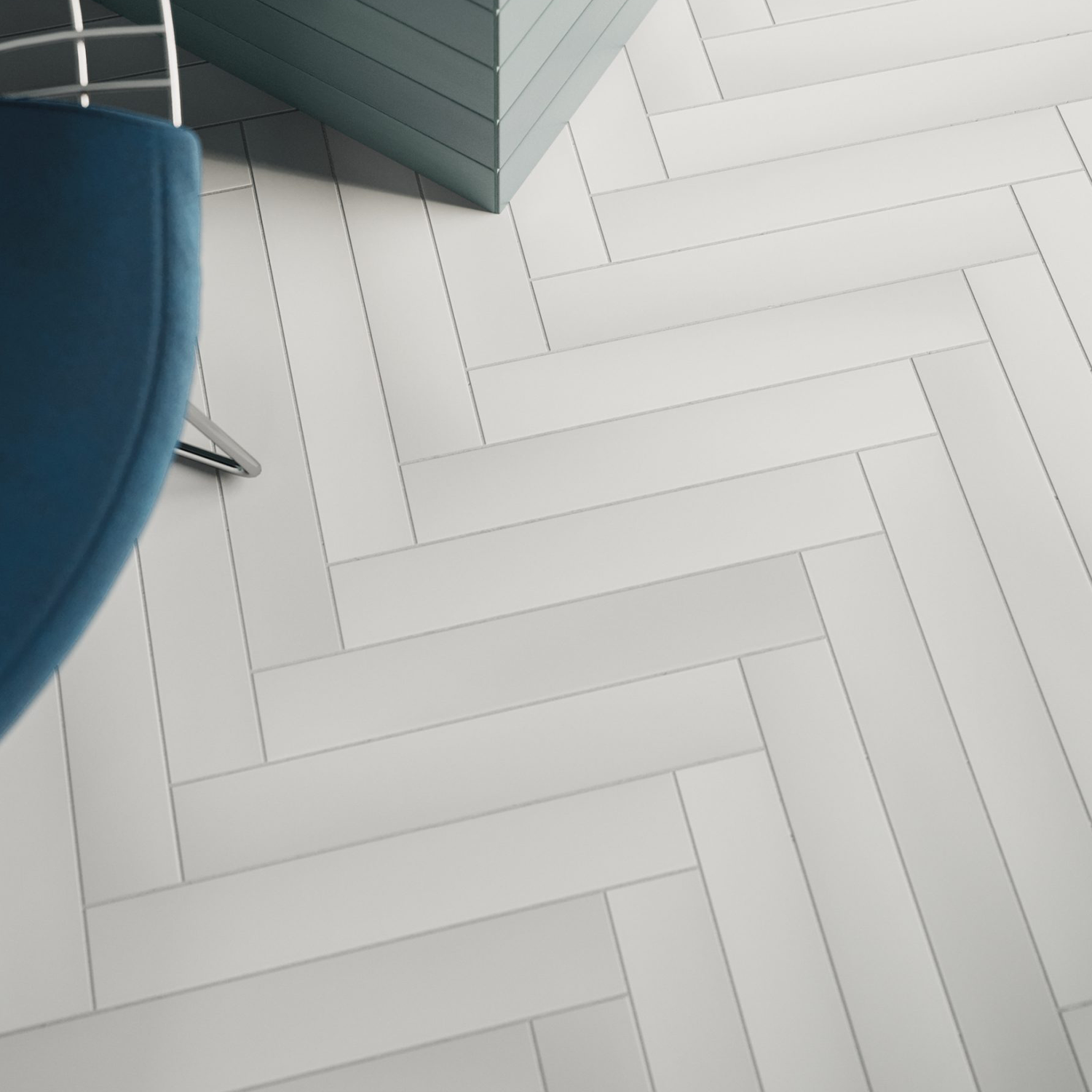 A floor tiled with Pigmento - Bianco in a herringbone pattern, with part of a blue chair and the corner of a teal cabinet visible at the top of the image.