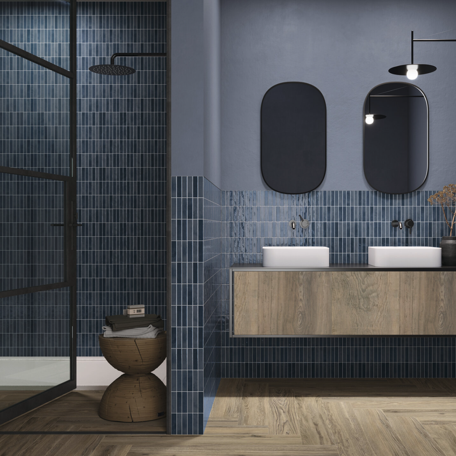Modern bathroom featuring Pim Pam Pum - Pim Blue tiled walls, a wooden floating vanity with two vessel sinks, dual oval mirrors, black fixtures, and a walk-in shower with glass door; decorative basket and dried flowers provide accent touches.