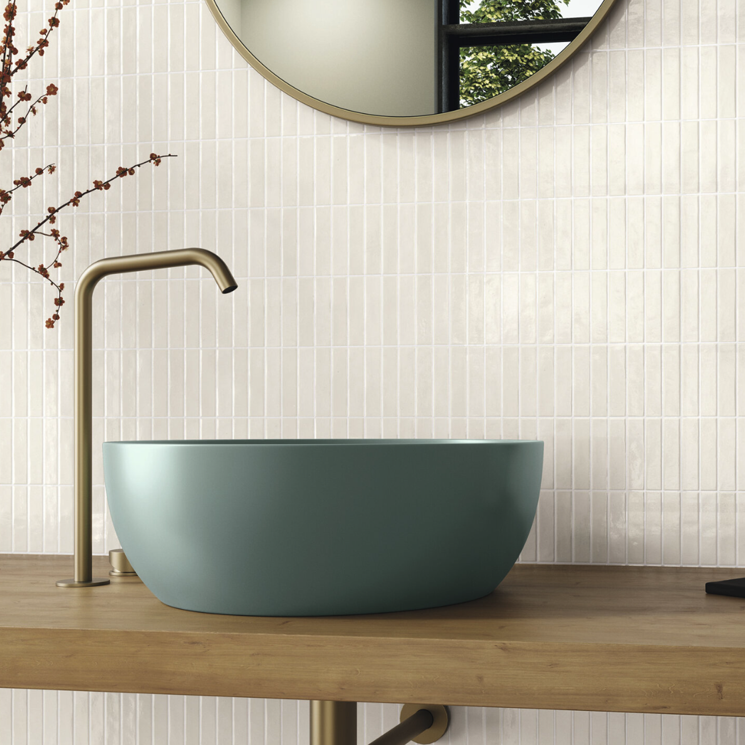A modern bathroom sink featuring the Pim Pam Pum - Pim White, paired with a matte blue basin, brass faucet, wooden countertop, and a round mirror above. A white vertically-tiled wall and a branch with small buds complete the minimalist aesthetic.