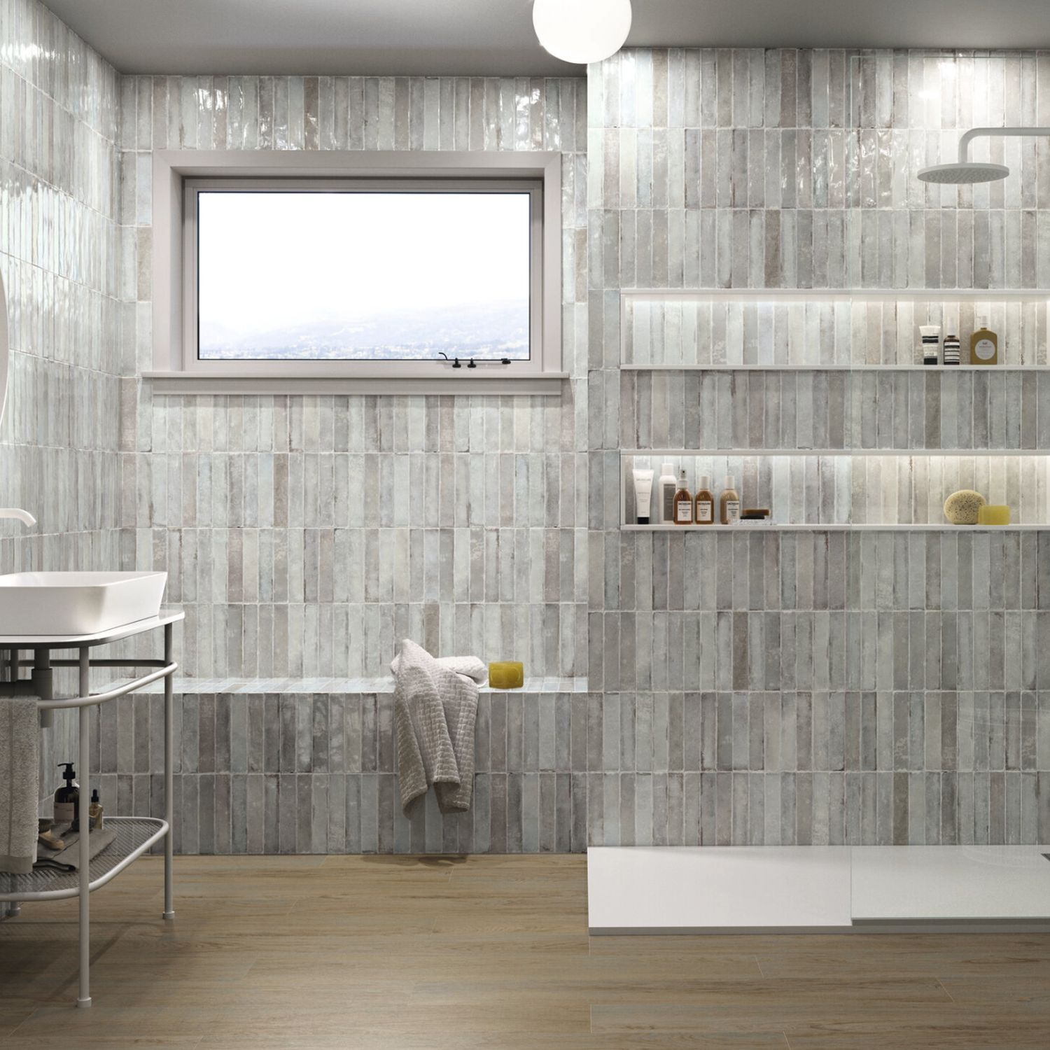 Modern bathroom featuring Savannah - Grey vertical tiles, wood flooring, built-in shelves with toiletries, a white sink, a walk-in shower, and a large window allowing natural light. A yellow towel is placed on the built-in bench.