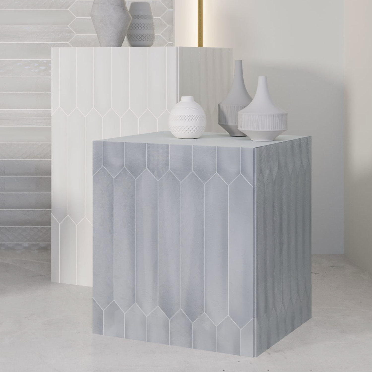 Two geometric pedestals, one white and one light blue, display white decorative vases against a backdrop featuring the Sfumature - Azzurro tile—a modern wall with subtle vertical patterns. The scene is minimalistic and contemporary.