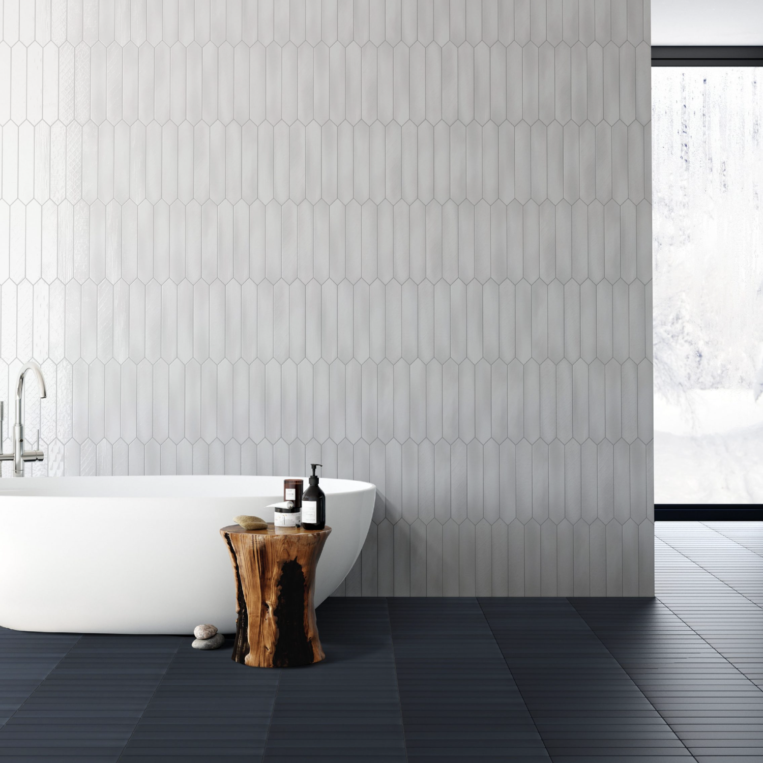 Modern bathroom featuring a white freestanding tub, Sfumature - Bianco light gray elongated wall tiles, dark floor tiles, a wooden stool, and a large window displaying a snowy outdoor scene.
