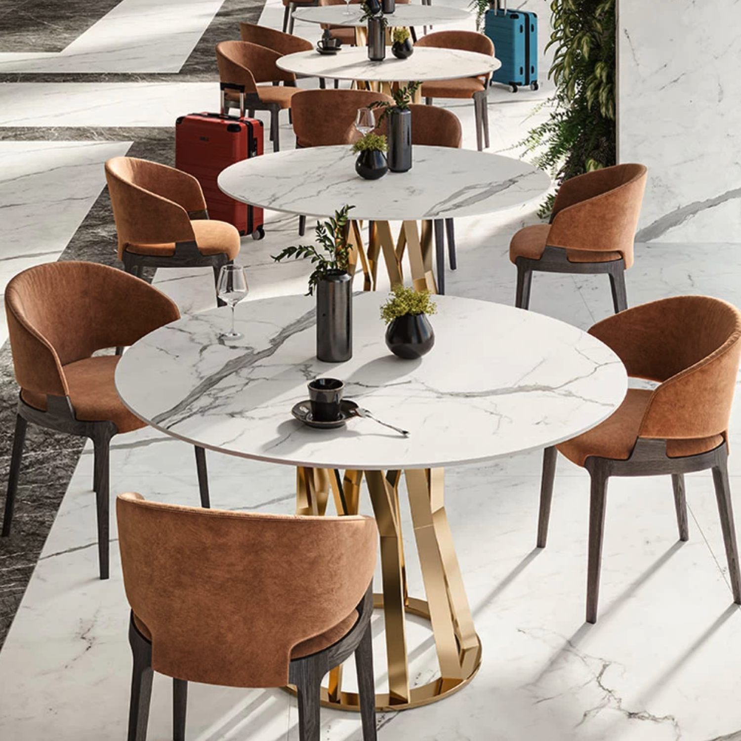 Contemporary cafe interior featuring round marble tables, brown chairs, black vases with plants, coffee cups, wine glasses, and colorful suitcases placed on a Statuario Supremo white marble floor with geometric patterns.