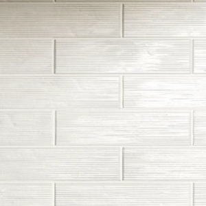 A kitchen counter is adorned with a bowl of pears, a black carafe, and a jar of flour. Above, a wooden shelf displays neatly stacked bowls and plates. The backsplash features Swing - White rectangular, textured tiles.