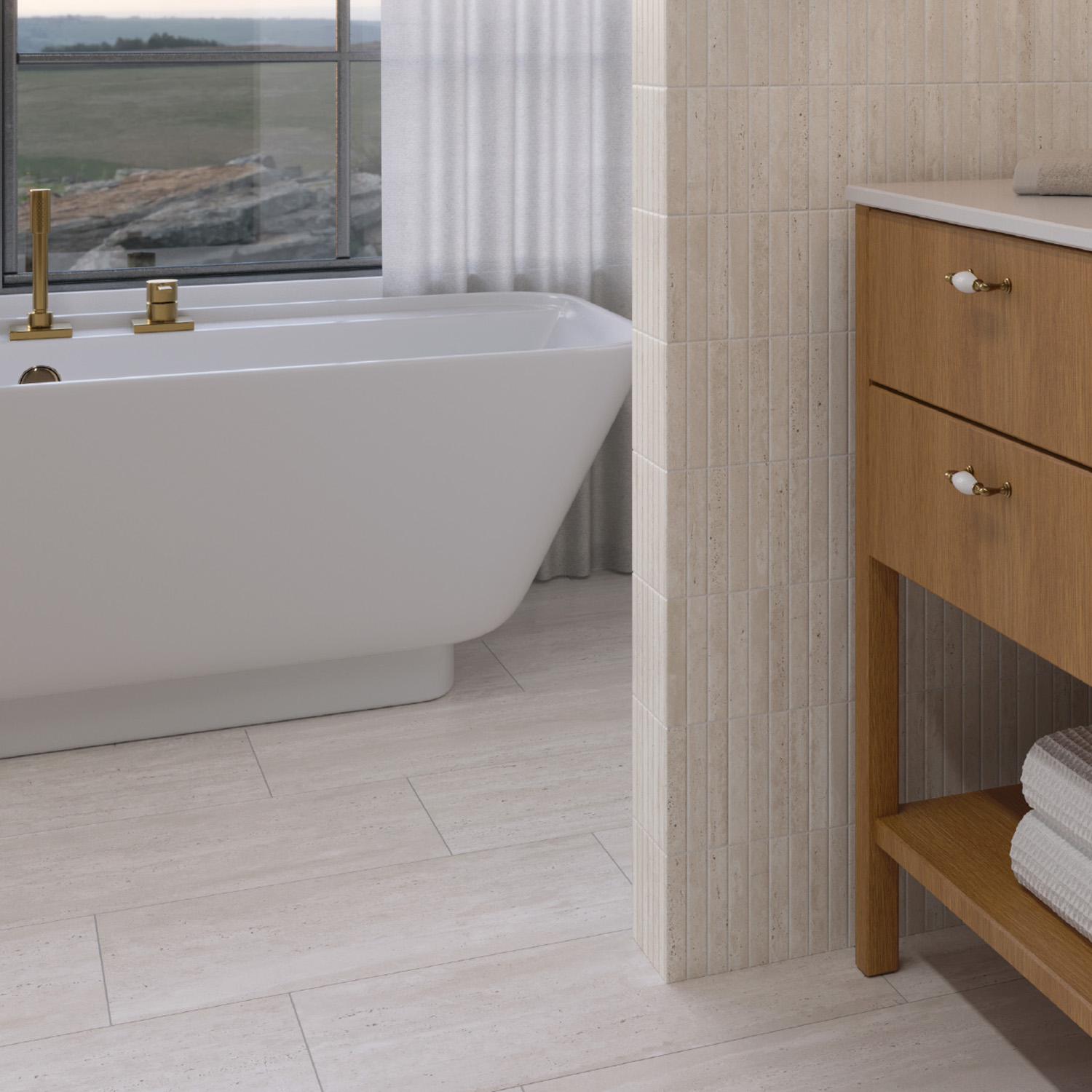 Modern bathroom featuring a white freestanding tub, gold fixtures, and elegant Travstone - Bone tile floors and walls. A wooden vanity with folded towels rests on the shelf, while a large window in the background bathes the space in natural light.