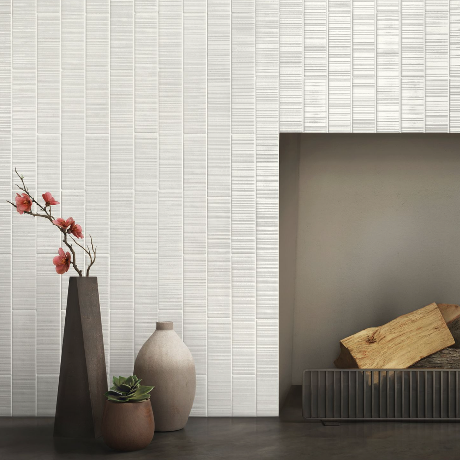 A minimalist interior features a textured Vibrant - White tile wall, with three vases—one tall filled with pink flowers, one round, and one housing a succulent—displayed beside a fireplace stacked with firewood.
