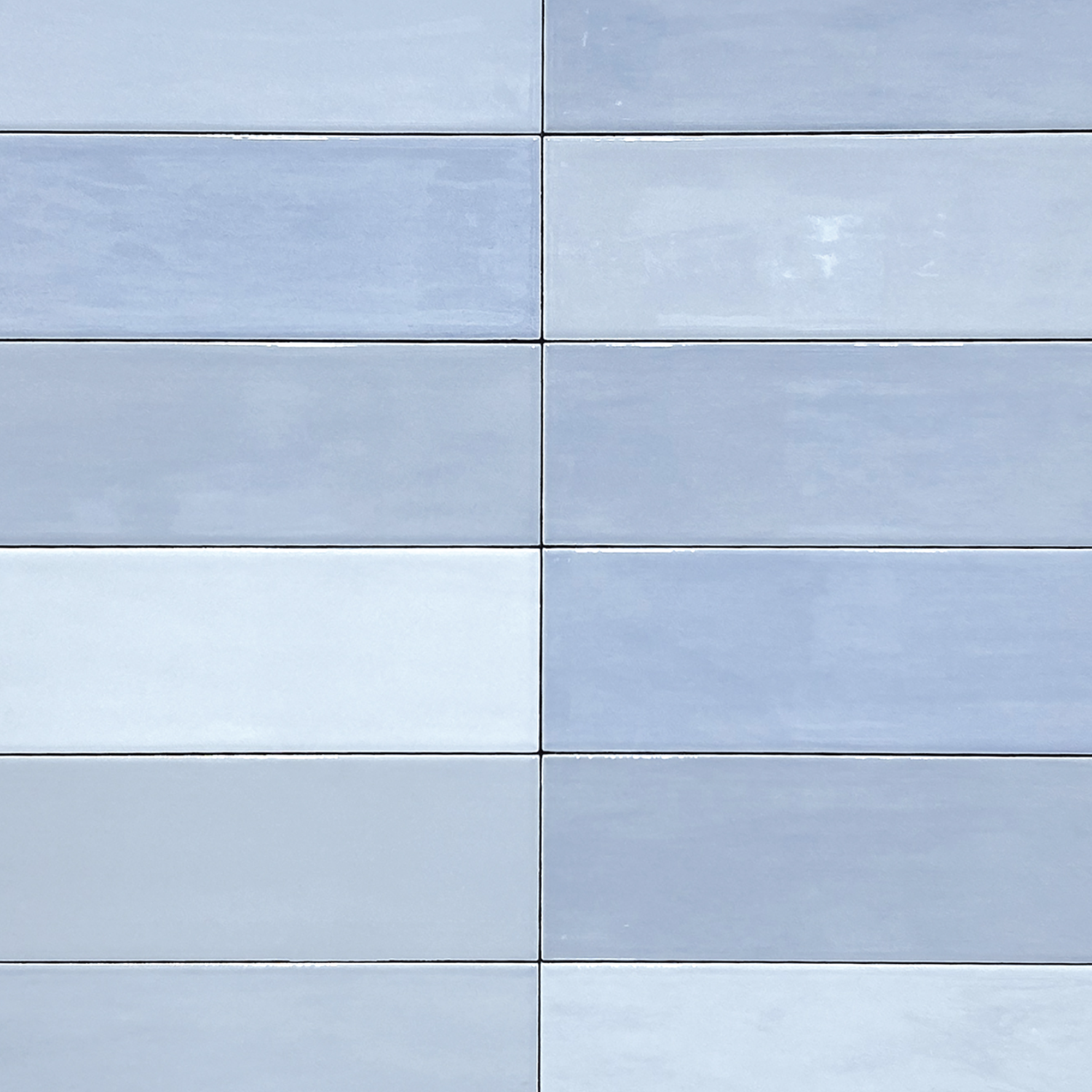 A close-up view of a wall covered with Zellige - Arctic large, rectangular, light blue tiles arranged in a grid pattern. Each tile features subtle color variations.