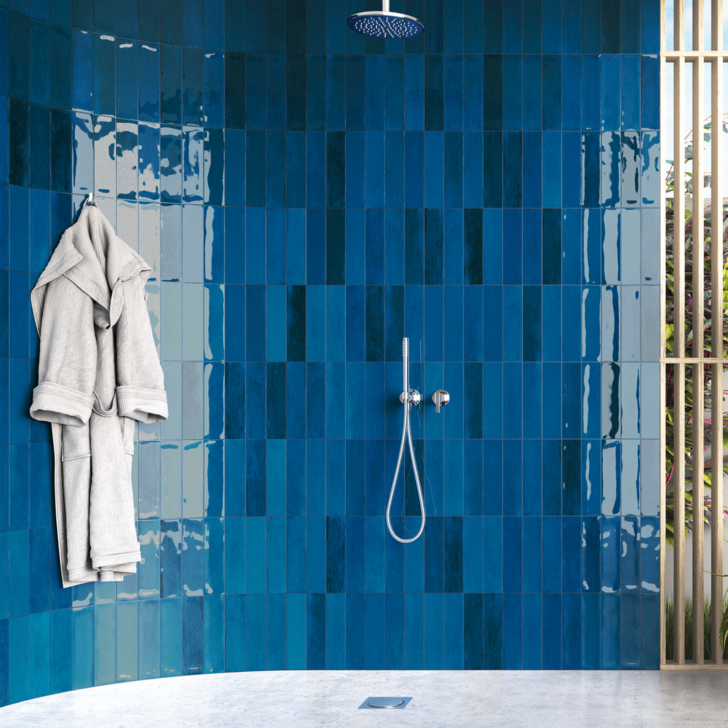 A modern shower featuring Zellige - Blue glossy tile walls, a rainfall showerhead, a white robe hanging on the left, and natural light streaming in through wooden slats on the right.