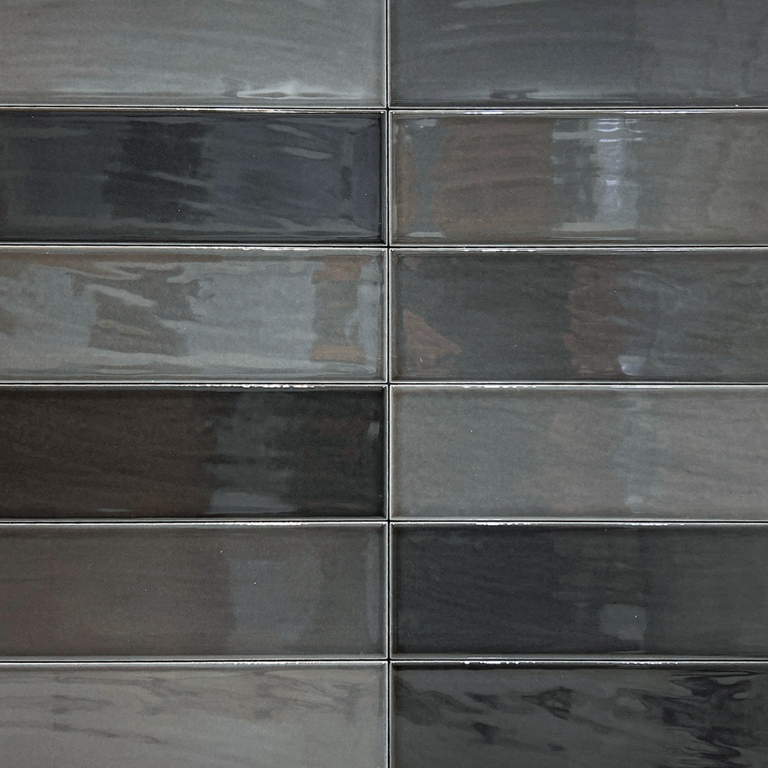 Zellige - Coal tiles feature a rectangular, glossy ceramic design in various shades of gray, arranged horizontally in a brick pattern. Their reflective surfaces with subtle streaks and gradients create a modern and sleek look.