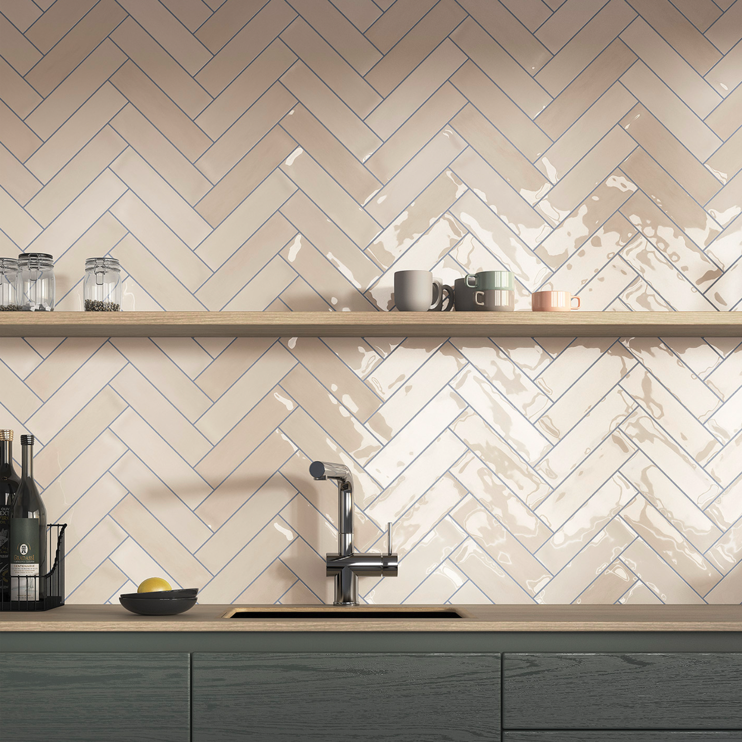 A modern kitchen backsplash featuring Zellige - Ivory glossy beige herringbone tiles, complemented by a wooden shelf holding cups and glasses, a sink with a faucet, and a countertop with a bowl, a lemon, and bottles.
