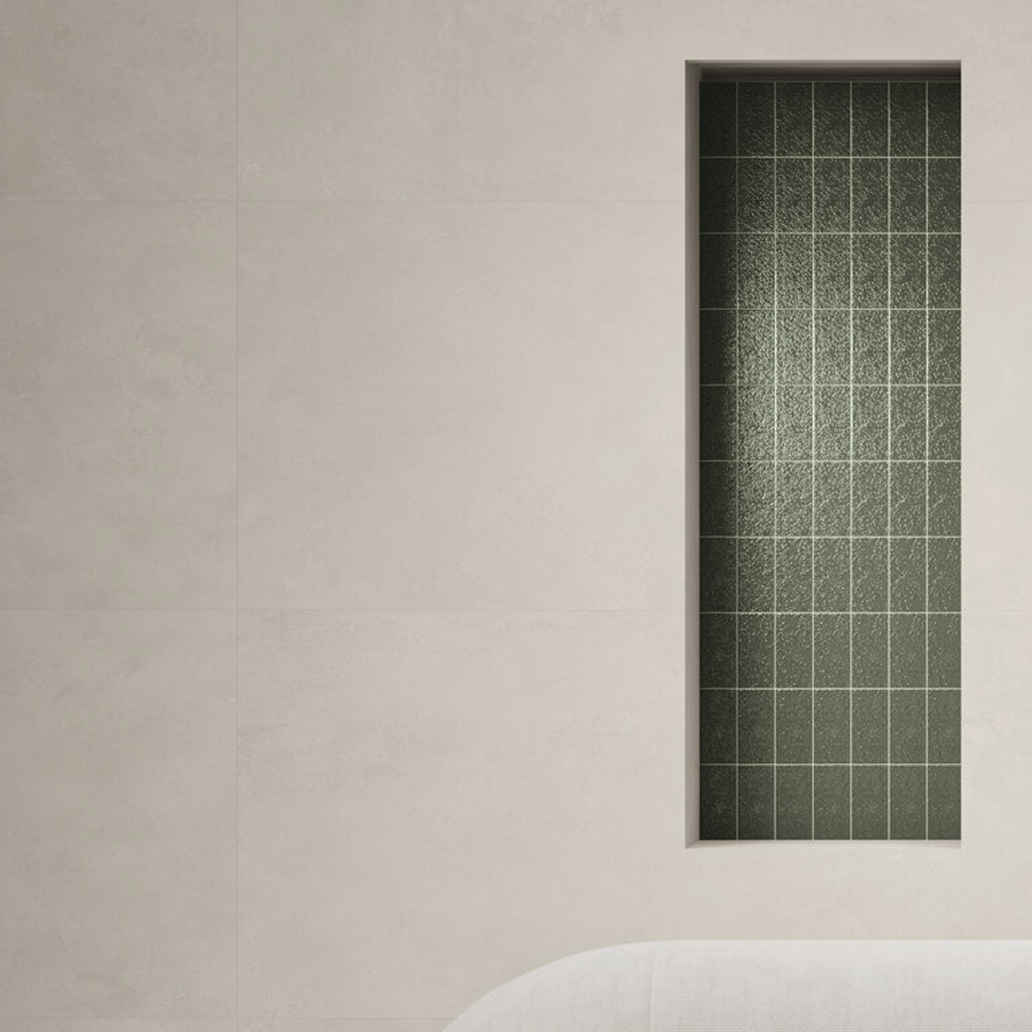 Minimalist interior wall with a tall, narrow rectangular recess clad in Arka - Green small dark tiles, situated beside a light gray or beige smooth wall and featuring the curved edge of a white sofa at the bottom.
