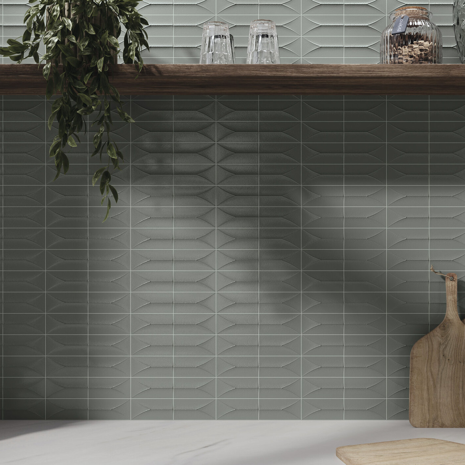 Arka - Forma Steel gray geometric-patterned tile backsplash with a wooden shelf above, displaying upside-down glasses and a leafy plant. Below, the countertop features a round wood board and a paddle-shaped board on the right side.