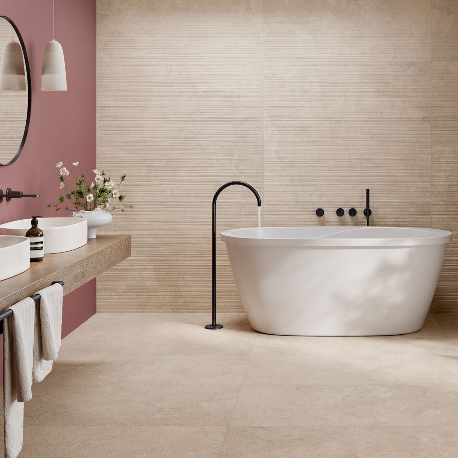 Modern bathroom featuring a freestanding white tub, wall-mounted black fixtures, a floating double vanity, towels, a round mirror, hanging lights, and a vase of flowers. The main walls are finished in Portland Rock - Beige with one accent wall in dusty rose.
