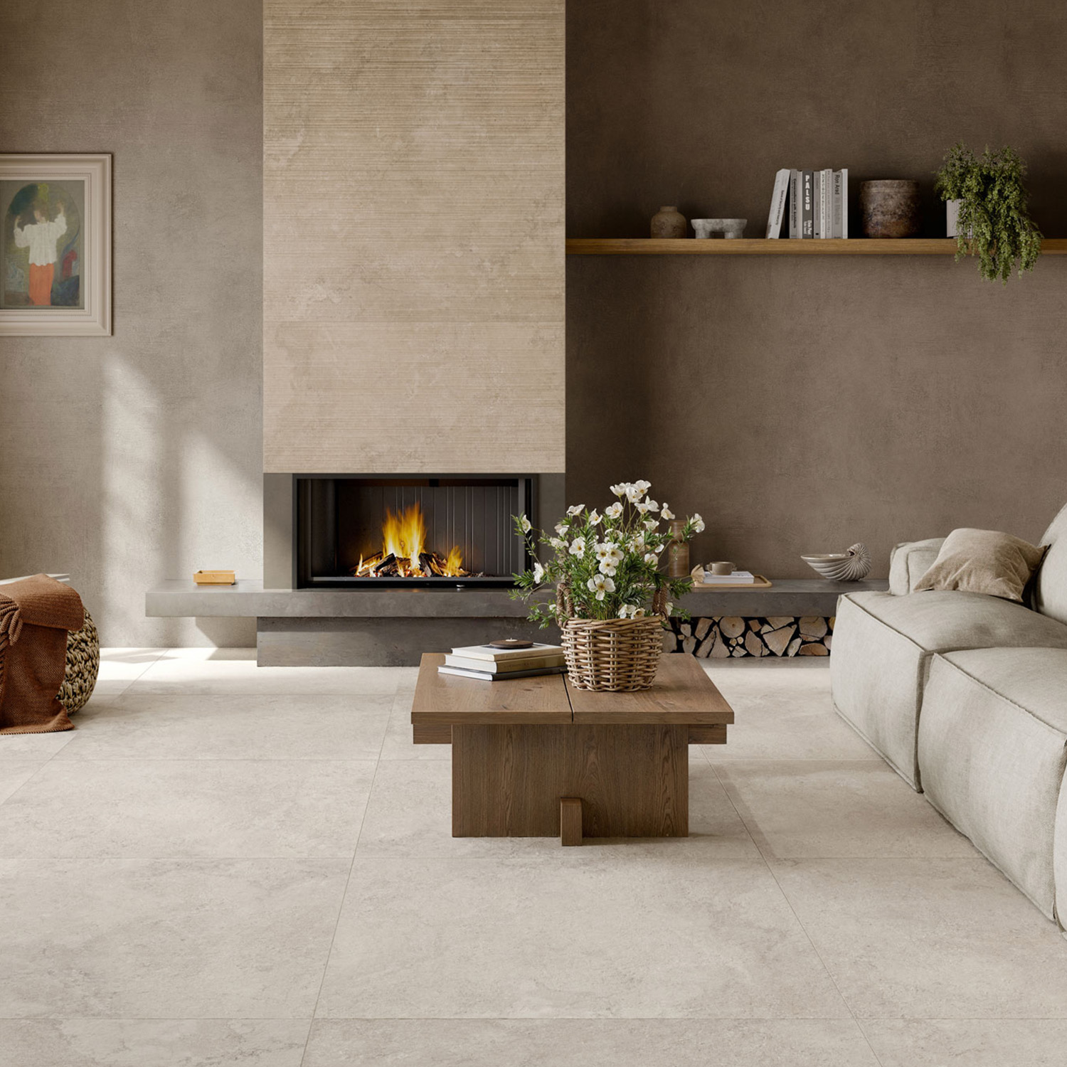 A modern living room features a stone-clad fireplace with a burning fire. Large Portland Rock - White floor tiles set the foundation for the space. In front of a beige sofa sits a low wooden coffee table adorned with a basket of white flowers. A shelf on the textured brown wall holds books and a plant.