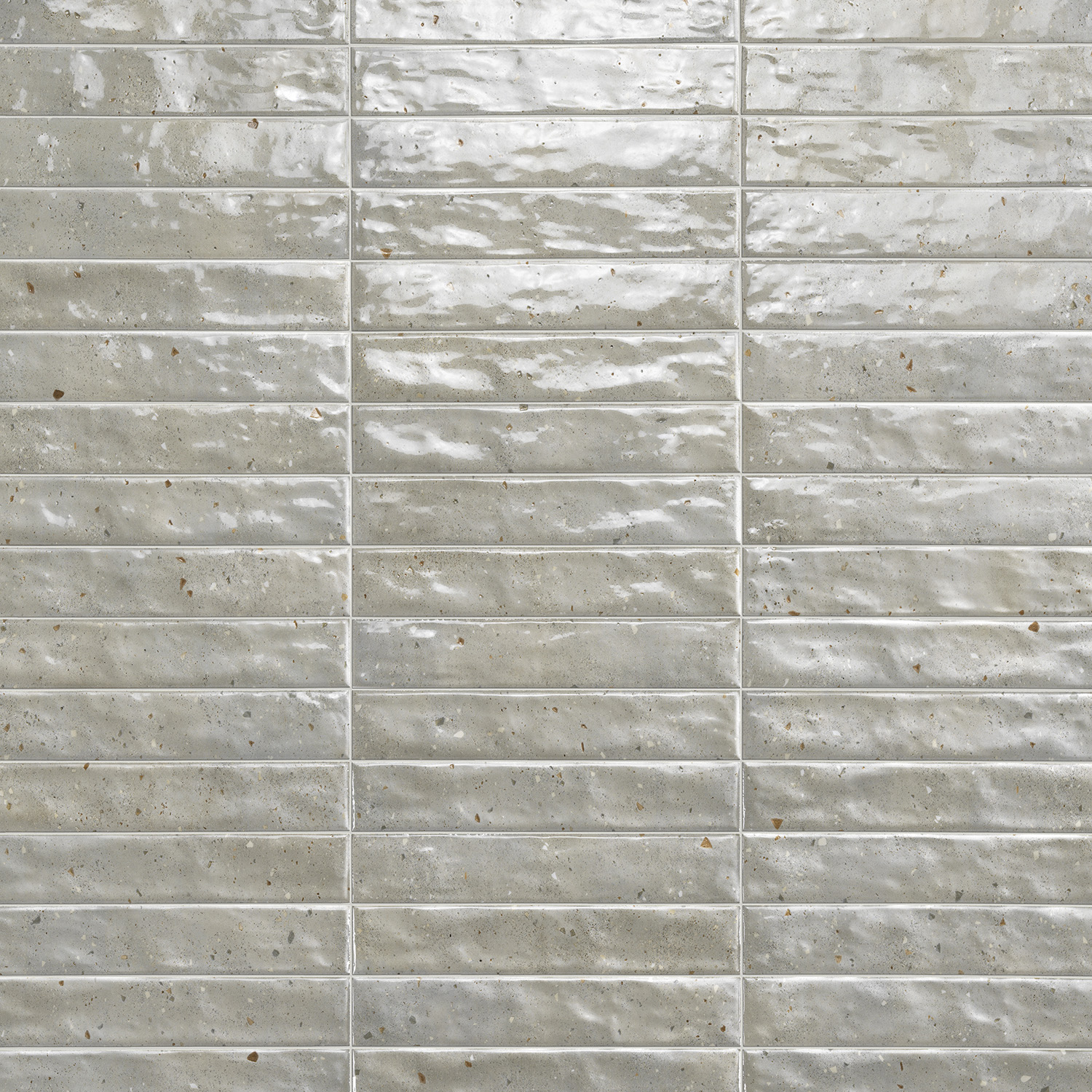 Via Del Sale - Mud ceramic tiles, featuring a glossy finish, rectangular shape, and light gray color with subtle speckles and uneven surfaces, are arranged horizontally in a grid pattern to create a textured wall.