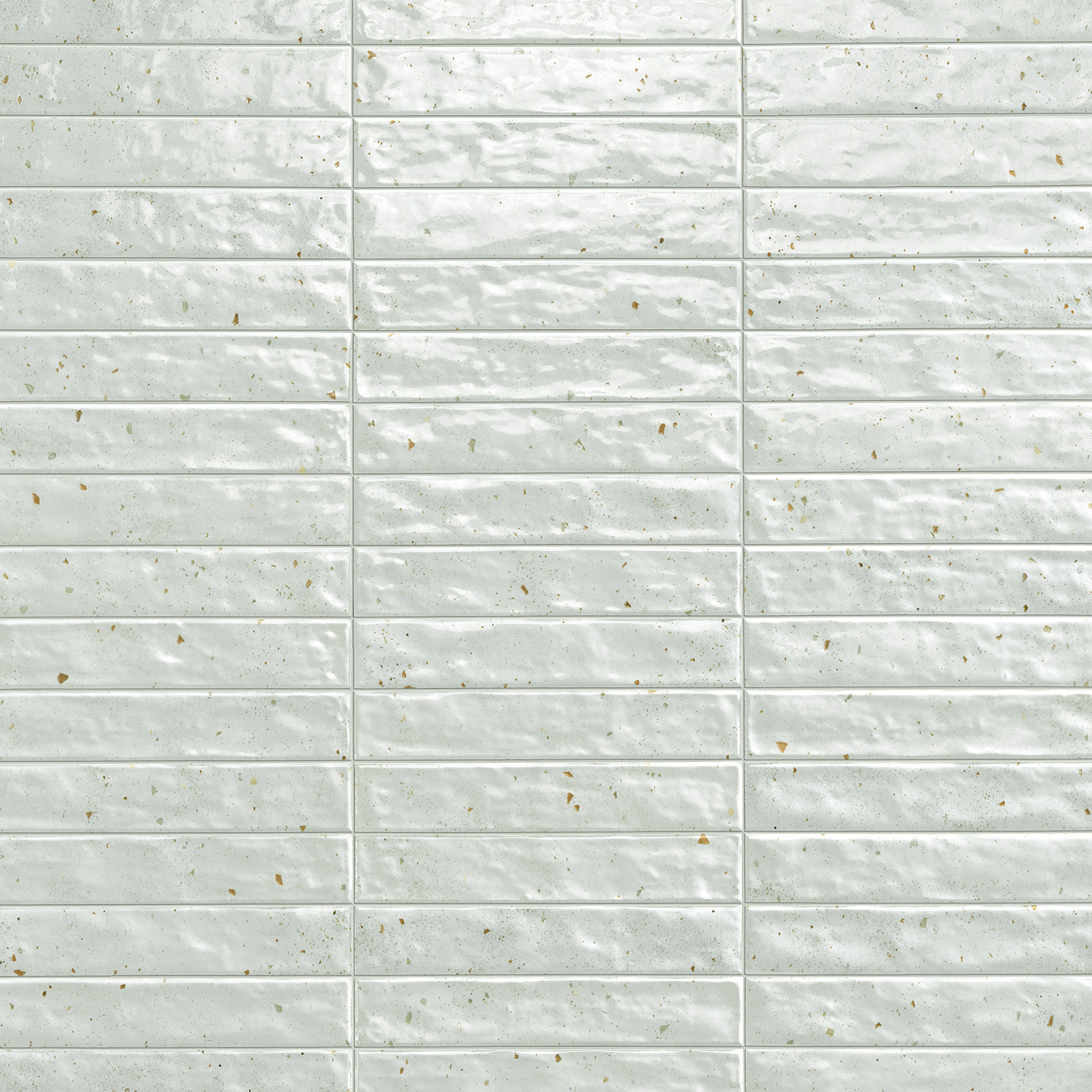 Glossy, sage green rectangular tiles from the Via Del Sale collection feature subtle speckles and uneven surfaces, arranged in a horizontal brick pattern. Light reflects off their textured finish, creating a varied, slightly wavy appearance.