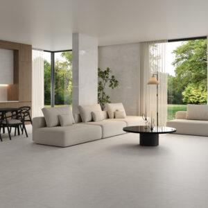 Modern living room with large windows, beige sofas, a round black coffee table, a floor lamp, Afyon Bianco flooring, and views of greenery outside. Dining area with black chairs visible in the background.