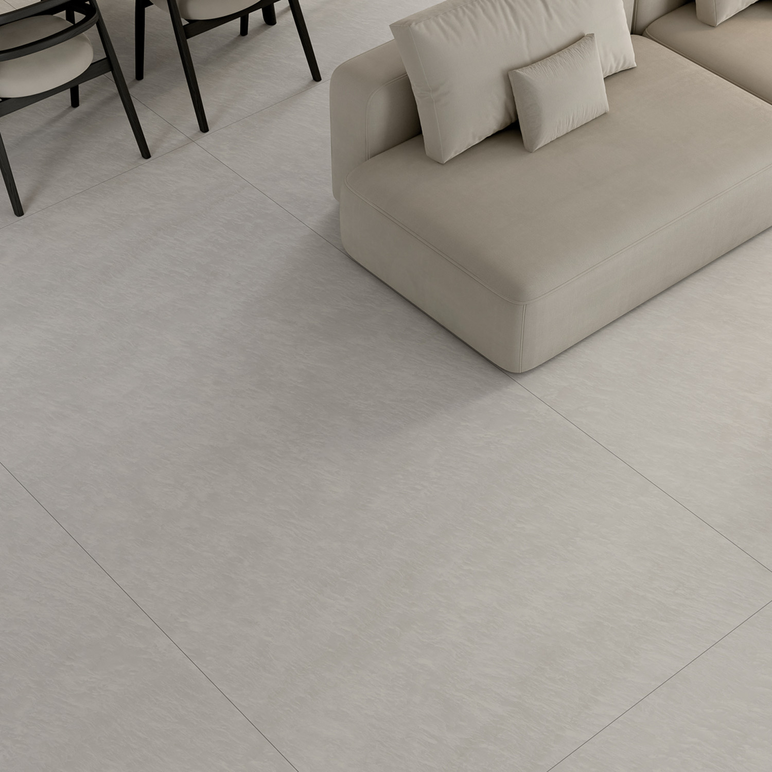 Minimalist living room with a light beige sectional sofa and cushions set atop a large expanse of Afyon Bianco tiles. In the background, black dining chairs and a table are partially visible.